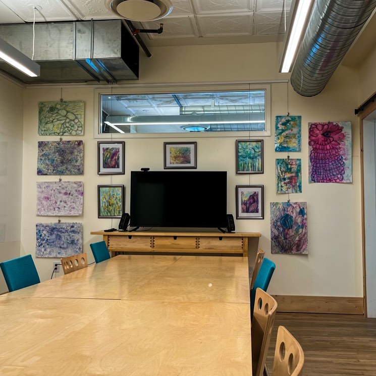 Colourful artwork on display in a room with table, chairs and large computer monitor.