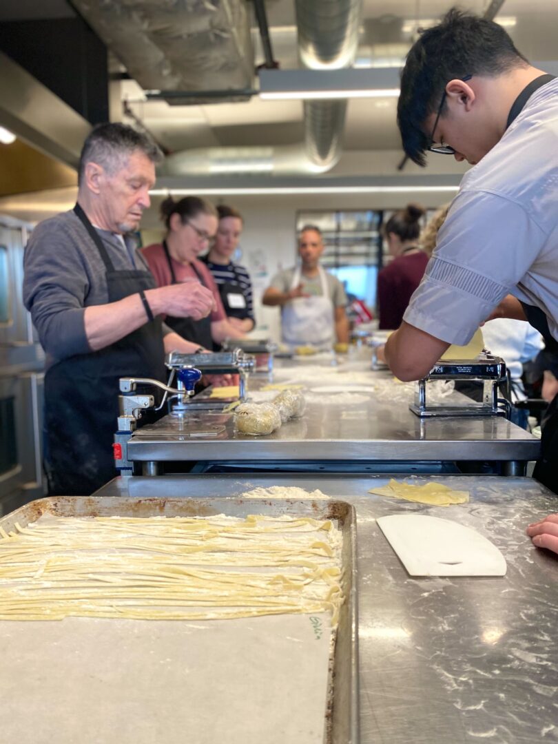 People making pasta on a metal counter together in a community kitchen