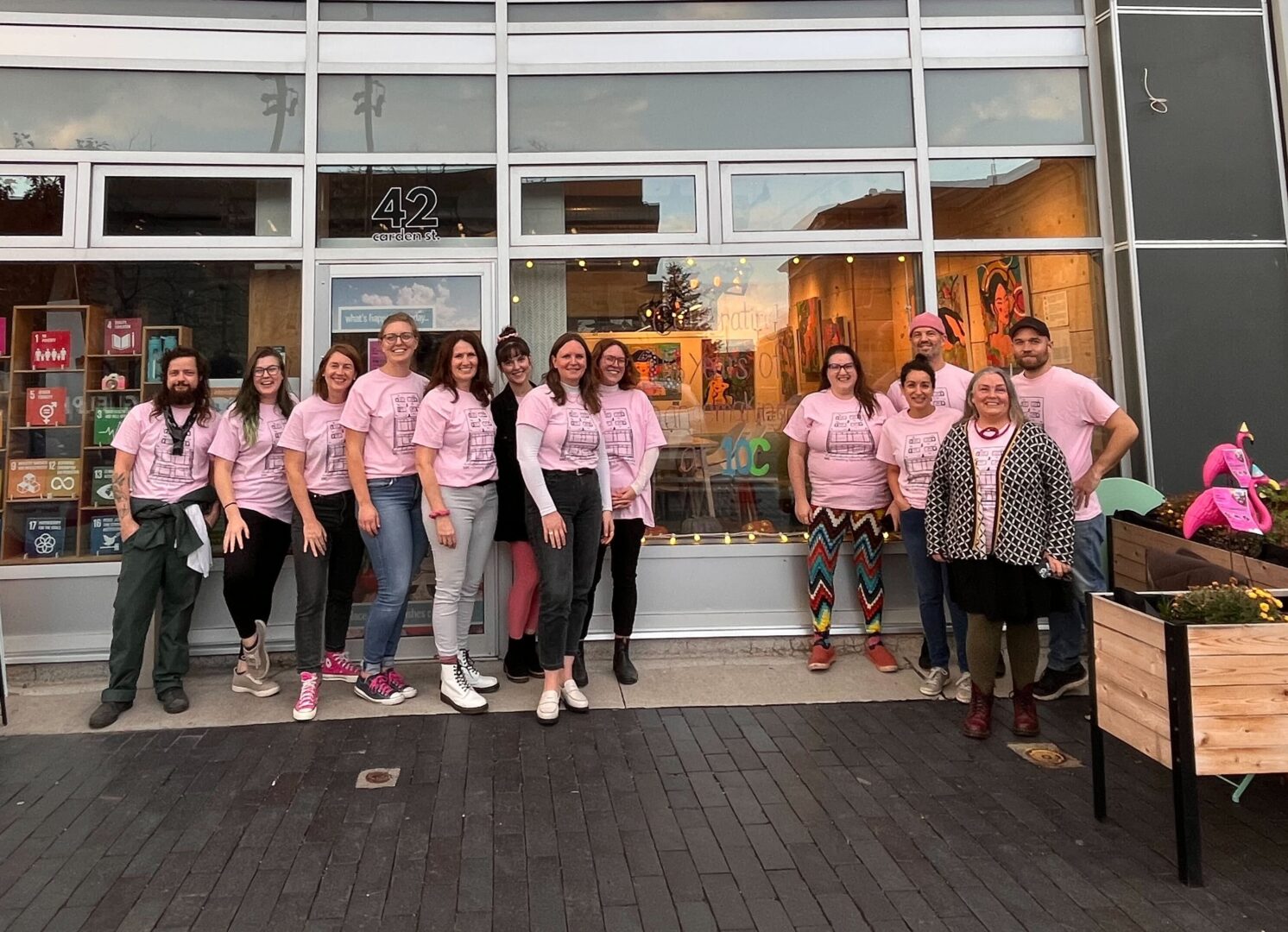 A group of people stand outside in front of a building wearing matching pink t-shirts.