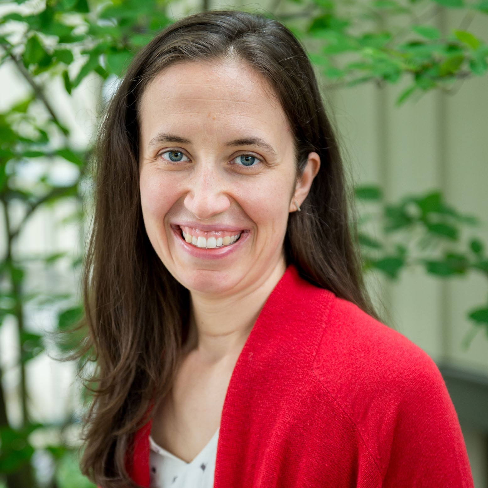 Woman with long brown hair in a white shirt and red sweater smiling at the camera.